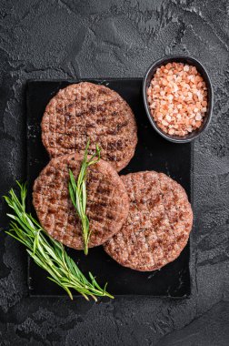 Beef burger patty cutlet for hamburger grilled on BBQ on marble board with rosemary. Black background. Top view.