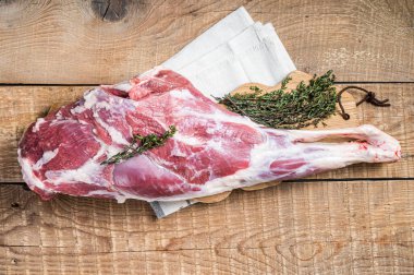 Butcher board with Raw lamb mutton leg with herbs. Wooden background. Top view.