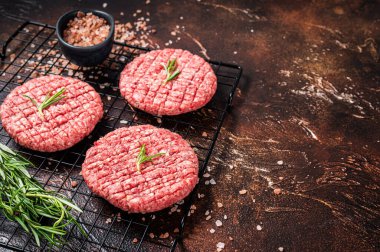 Raw burger cutlet from beef meat with spices and rosemary ready for cooking. Dark background. Top view. Copy space.