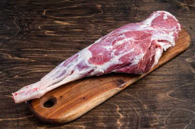 Mutton meat. Raw whole lamb leg thigh on butcher board. Wooden background. Top view.