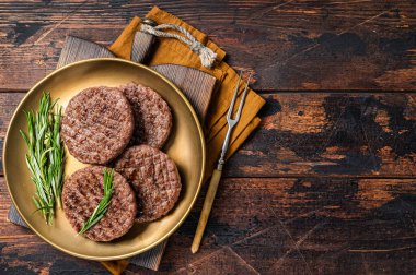 Grilled burger beef meat patty with herbs and spices on steel plate. Wooden background. Top view. Copy space.