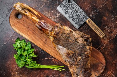 Roast lamb leg meat with herbs and spices on a cutting board. Dark background. Top view.