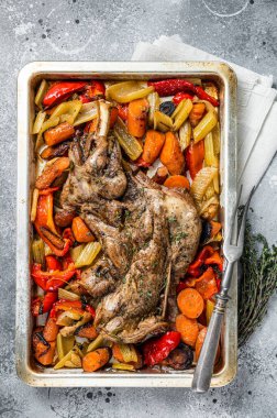 Roast lamb mutton shoulder meat in a baking dish with vegetables. Gray background. Top view.