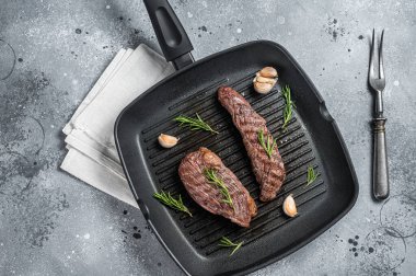 Roasted on a grill skillet Flank flap or Bavette beef meat steak with rosemary. Gray background. Top view.