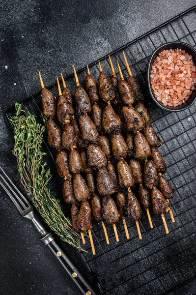 Grilled shish kebab with chicken hearts on a grill. Black background. Top view.