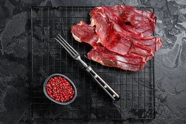Dried sliced basturma, cured beef meat ready for eat. Black background. Top view.