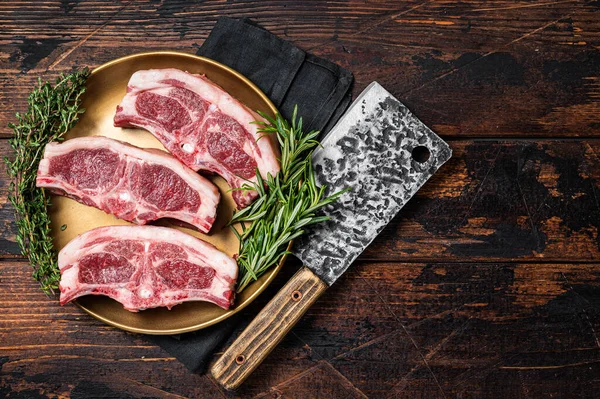 Uncooked Raw lamb loin chops steaks, saddle in plate with rosemary and thyme. Wooden background. Top view. Copy space.