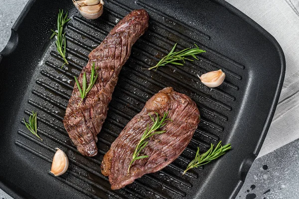 Roasted on a grill skillet Flank flap or Bavette beef meat steak with rosemary. Gray background. Top view.