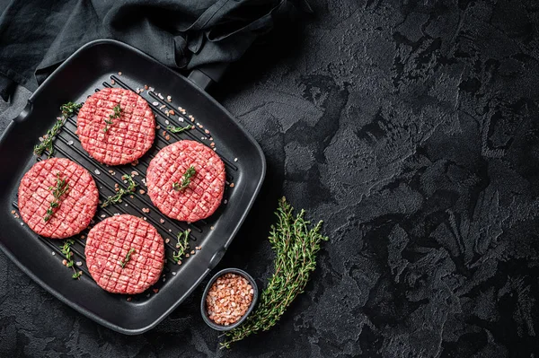 Raw Ground beef meat Burger steak cutlets in grill skillet ready for cooking. Black background. Top view. Copy space.