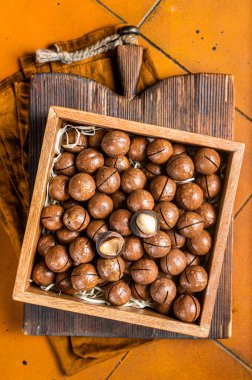 Macadamia natural nuts in a box. Orange background. Top view.