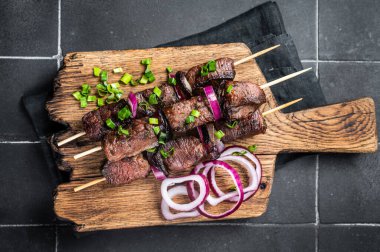 Shashlik grilled meat skewers, shish kebab with beef and lamb meat, onion and herbs. Black background. Top view.