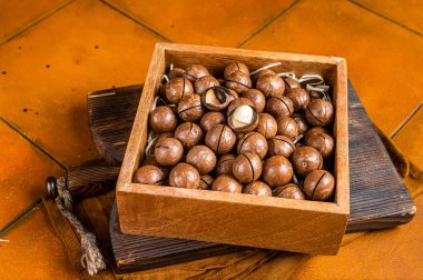 Macadamia natural nuts in a box. Orange background. Top view.