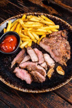 Roast BBQ pork chop steak on plate with potato chips. Wooden background. Top view.
