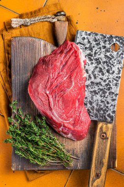 Piece of Raw beef meat for stew with herbs on butcher cutting board. Orange background. Top view.