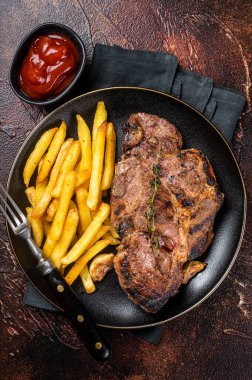 Roasted pork steaks from neck meat in plate with potato chips. Dark background. Top view.