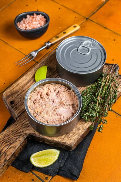Tin with Canned tuna fillet meat in olive. Orange background. Top view.
