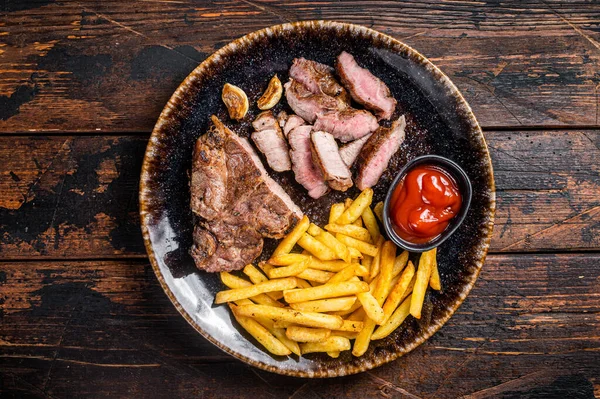 Roast BBQ pork chop steak on plate with potato chips. Wooden background. Top view.