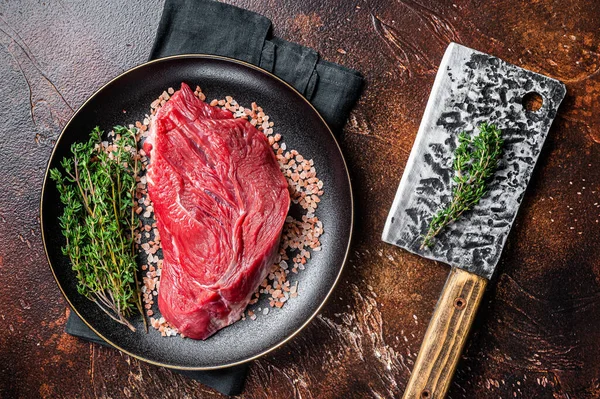 Raw beef sirloin steak with herbs and salt. Dark background. Top view.