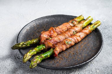Plate with pork bacon wrapped asparagus on grey table. White background. Top view.