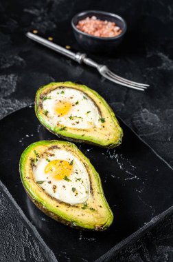 Eggs baked in avocado with herbs and spices. Black background. Top view.