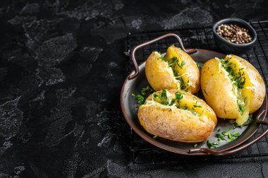 Baked Jacket potatoes with cheese, herbs and butter. Black background. Top view. Copy space.