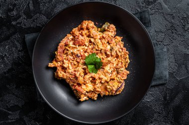 Turkish Menemen, Eggs with tomatoes, green peppers and green onion. Black background. Top view.