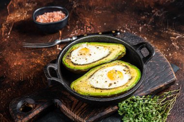 Baked Avocado with Egg, Salt, thyme and Pepper. Dark background. Top view.