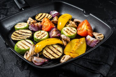 Vegetables grilled in a grill skillet, bell pepper, zucchini, eggplant, onion and tomato. Black background. Top view.