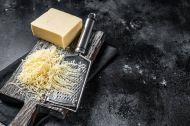 Grated cheese for cooking on a cutting board . Black background. Top view. copy space.