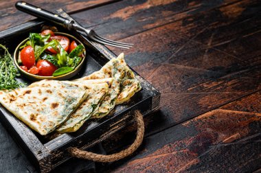 Baked Gozleme flatbread with greens in a box with vegetable salad. Wooden background. Top view. Copy space.