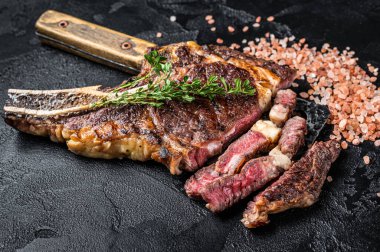 Dry aged grilled Tomahawk or cowboy beef meat steak on a meat cleaver. Black background. Top view.