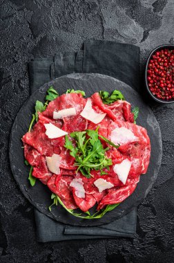 Beef carpaccio with arugula, parmesan cheese. Black background. Top view.