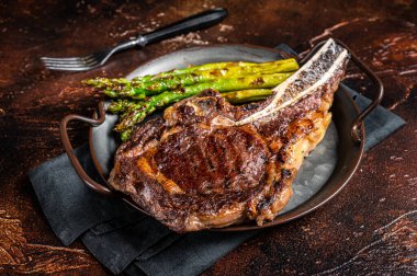 BBQ Grilled Tomahawk or Cowboy with bone beef steak, roasted asparagus. Wooden background. Top view.