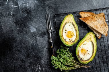 Cooking Baked Avocado with Egg. Black background. Top view. Copy space.