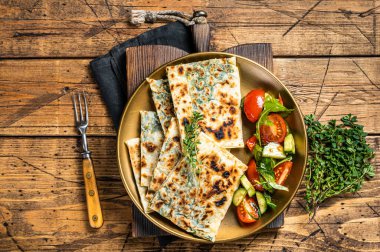 Gozleme flatbread with greens and vegetable salad on garnish. Wooden background. Top view.