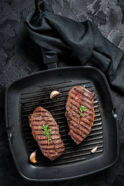 Grilled Top Blade or flat iron roast beef meat steaks on a skillet. Black background. Top View.