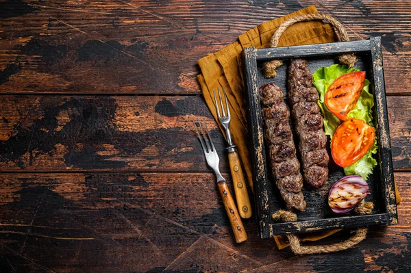 Traditional middle east kefta or kofta kebab, ground beef and lamb meat grilled on skewers served with tomato, salad and onion. Wooden background. Top view. Copy space.
