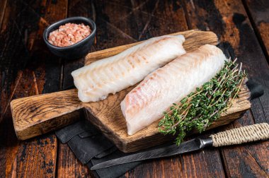 Cod fish fillets, raw codfish with thyme on wooden board. Wooden background. Top view.