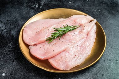Uncooked Raw chicken chop breast fillets on a plate, poultry meat. Black background. Top view.