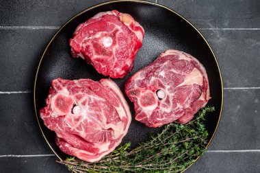 Raw Lamb Gerdan, lamb neck chops on a plate with herbs. Black background. Top view.