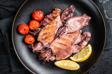 Seafood diner with grilled squid, calamary in a plate. Black background. Top view.