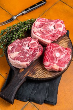 Raw lamb neck chops, fresh mutton meat on a butcher board with herbs. Orange background. Top view.