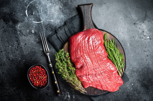 Raw flank beef steak, uncooked meat with herbs. Black background. Top view.
