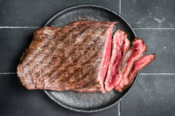 Grilled Flap or Flank Steak, sliced on a plate. Black background. Top view.