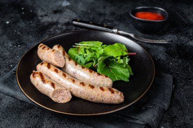BBQ Grilled pork sausages served with greens. Black background. Top view.
