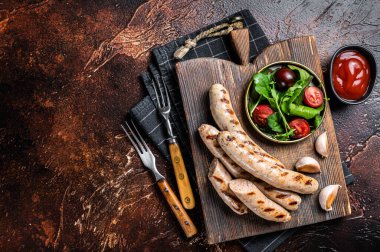 BBQ fried pork meat sausages served with greens on wooden board. Dark background. Top view. Copy space.