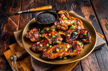 Teriyaki chicken wings with black sesame in a plate. Wooden background. Top view.
