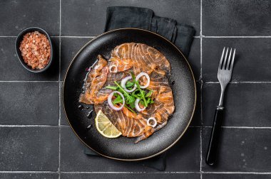Fresh Salmon carpaccio with onion and arugula on a plate. Black background. Top view.