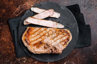 Roast BBQ pork Chop or T-bone meat steak sliced on a board. Dark background. Top view.