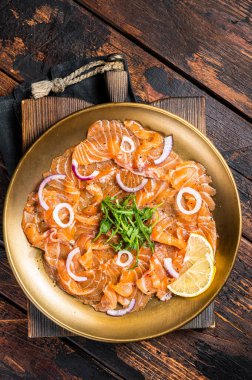 Italian Salmon carpaccio with onion and arugula served on a plate. Wooden background. Top view.